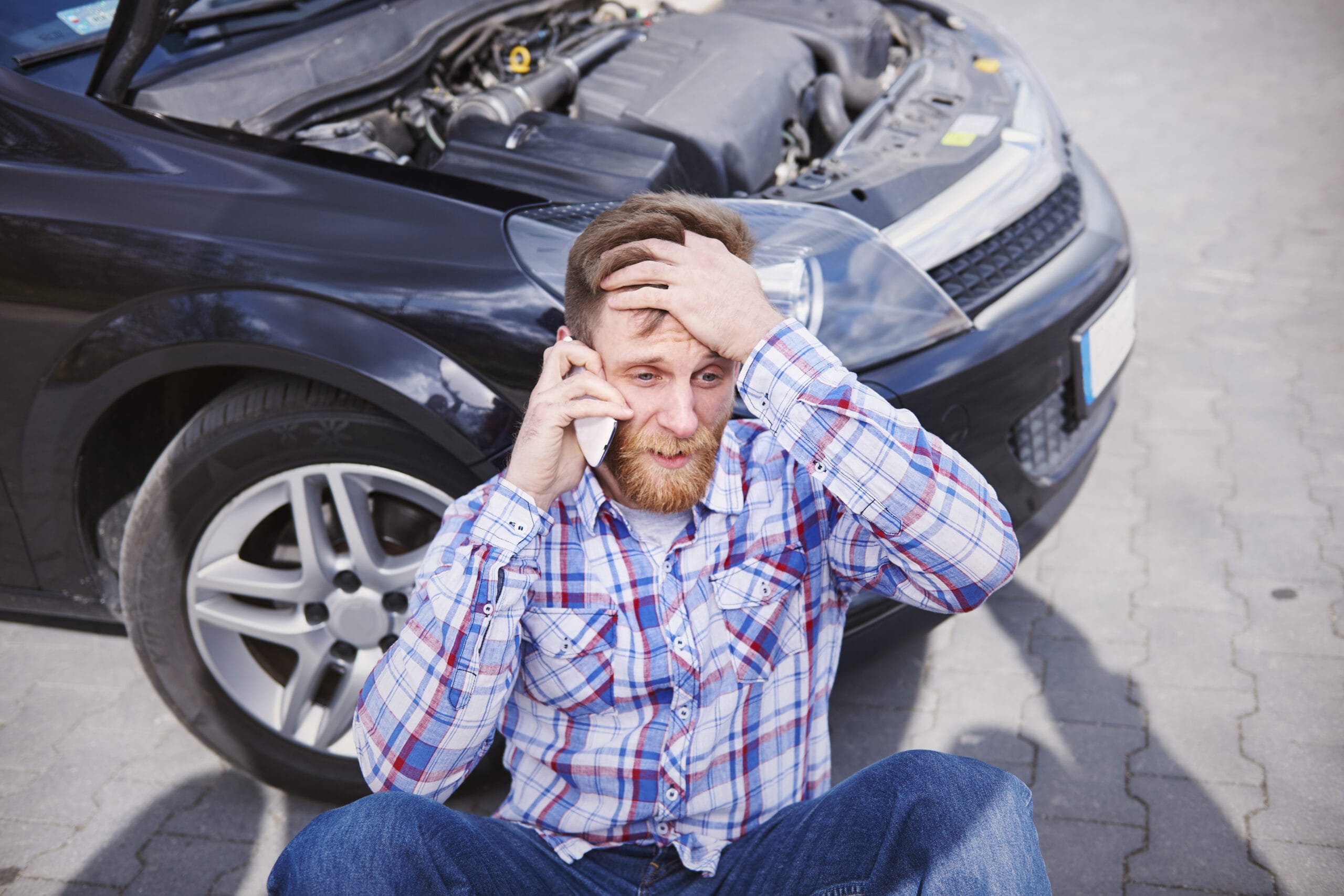 A person looking stressed on the phone as they are having problems with their car