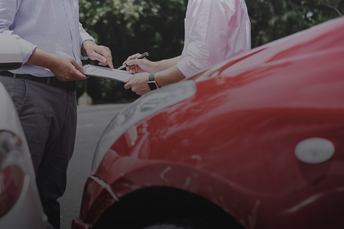 Two people reviewing papers in front of a damaged vehicle after an accident